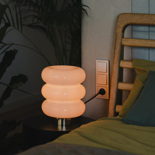 stojąca lampa bibe z mosiężnym wykończeniem przy łóżku zapalona świeci