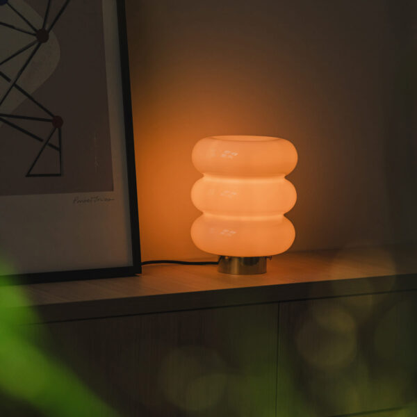 stojąca lampa bibe z mosiężnym wykończeniem przy łóżku zapalona świeci